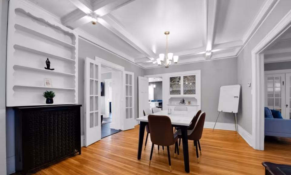 Bright dining room with a white table and brown chairs, built-in shelving, chandelier, and hardwood floors.