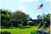Exterior view of a senior living facility with flag, manicured lawn, and trees.