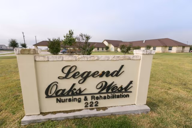 Entrance sign reading 'Legend Oaks West Nursing & Rehabilitation 222' on a grassy lawn with single-story facility buildings in the background.