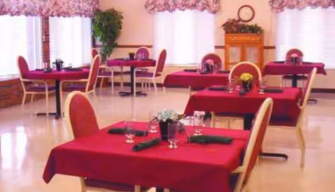 Senior living facility dining room with red tablecloths and large windows.