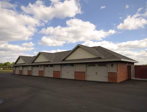 Row of cottage-style garages with pitched roofs and brick accents along a paved lot.