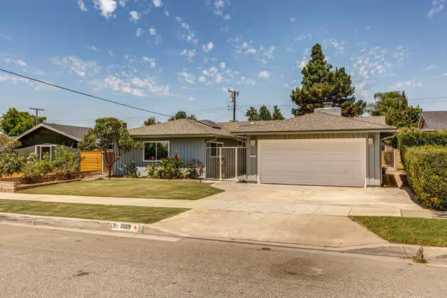 Single-story ranch-style house with an attached two-car garage, front lawn, and driveway under a blue sky.