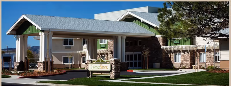 Front exterior of CornerStone assisted living showing the building entrance with a covered porte-cochère, stone sign, and landscaped lawn.