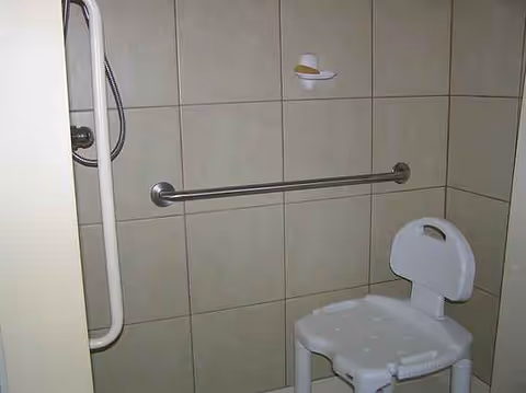 Accessible bathroom featuring a shower chair, grab bars, and tiled walls.