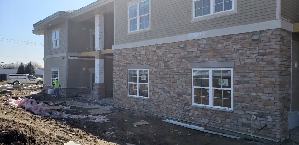 Front exterior of the Stonebay Senior Living building under construction showing stone veneer walls, windows, construction materials, and workers.
