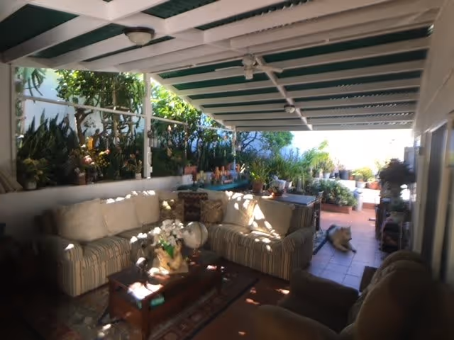 Covered outdoor patio with a cushioned sectional sofa, coffee table, potted plants and tiled floor.