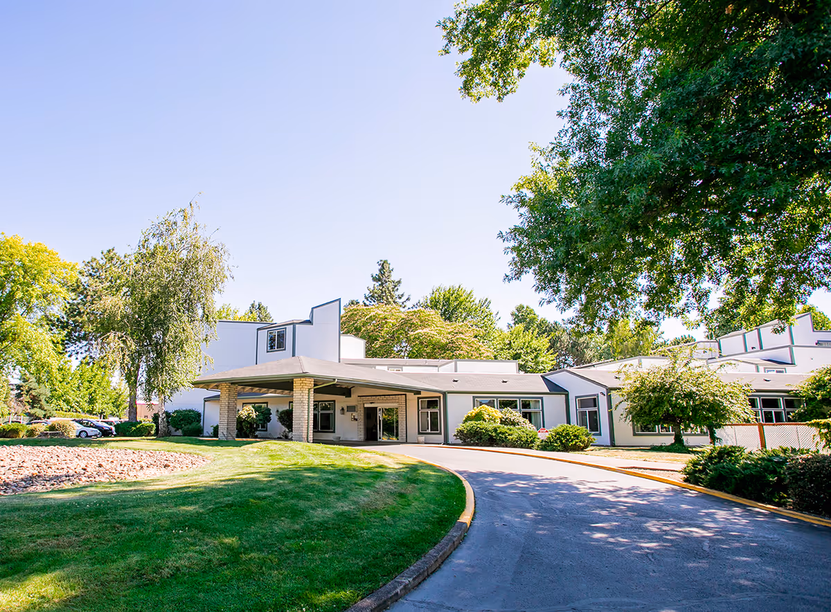 Exterior view of a modern white senior living facility with a curved driveway and well-kept landscaping.