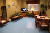 Communal lounge with wooden chairs and tables, a television, plants, and a window.