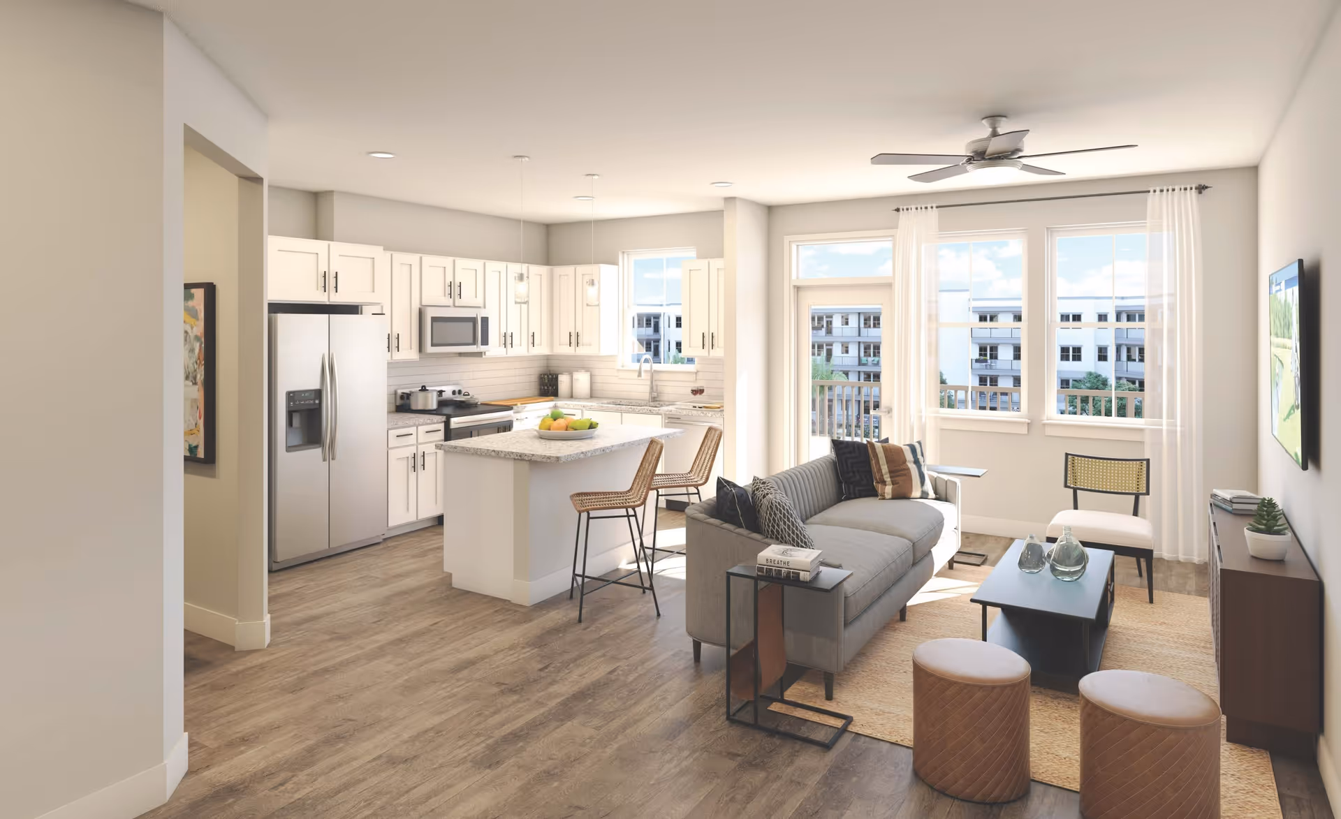 Bright and modern open-concept living space featuring a kitchen with white cabinets, stainless steel appliances, and a central island with two bar stools. Adjacent living room area includes a gray sofa with pillows, a coffee table, two round ottomans, a chair, and a TV mounted on the wall. Large windows and a glass door provide natural light and a view of neighboring buildings.