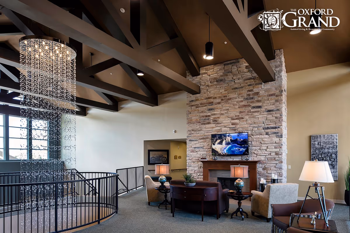 Spacious lounge with seating around a fireplace and TV, a cascading crystal chandelier, and exposed wooden ceiling beams.