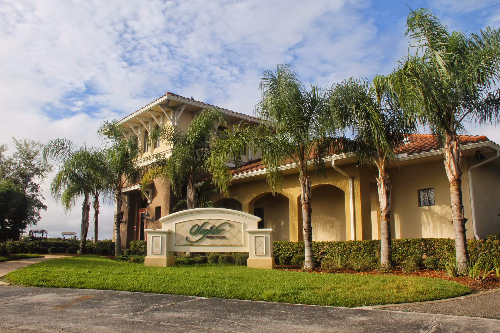 Mediterranean-style building entrance with palm trees and a decorative sign on a grassy lawn.