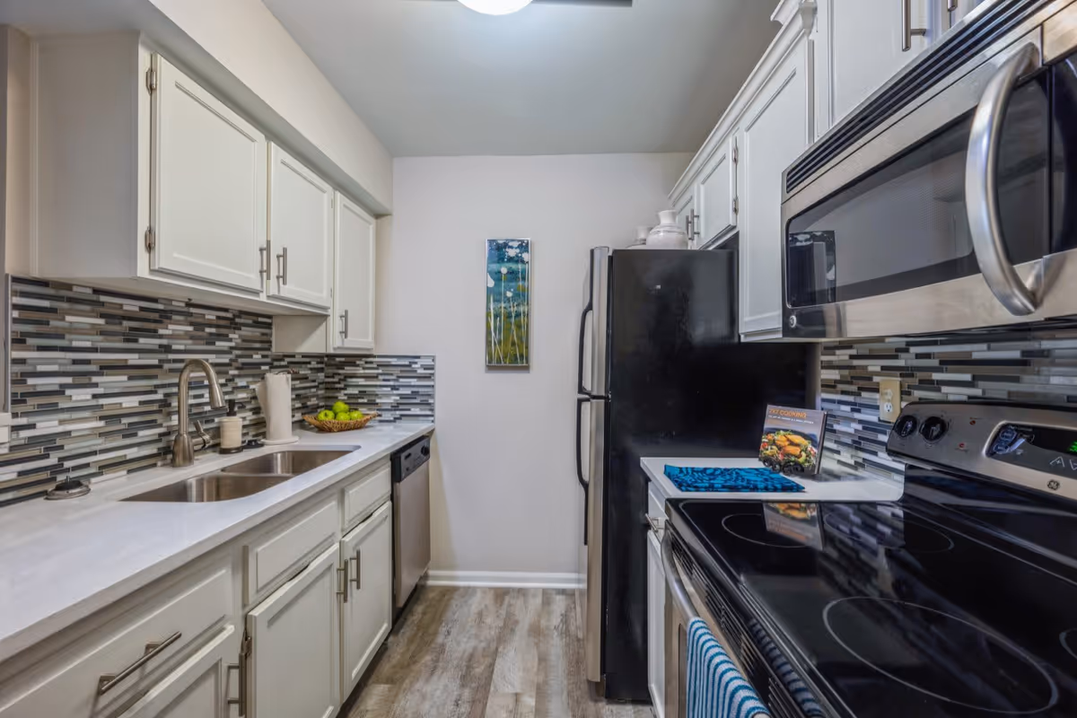A modern galley kitchen with white cabinets, mosaic tile backsplash, stainless steel appliances, and a double sink along the left counter.