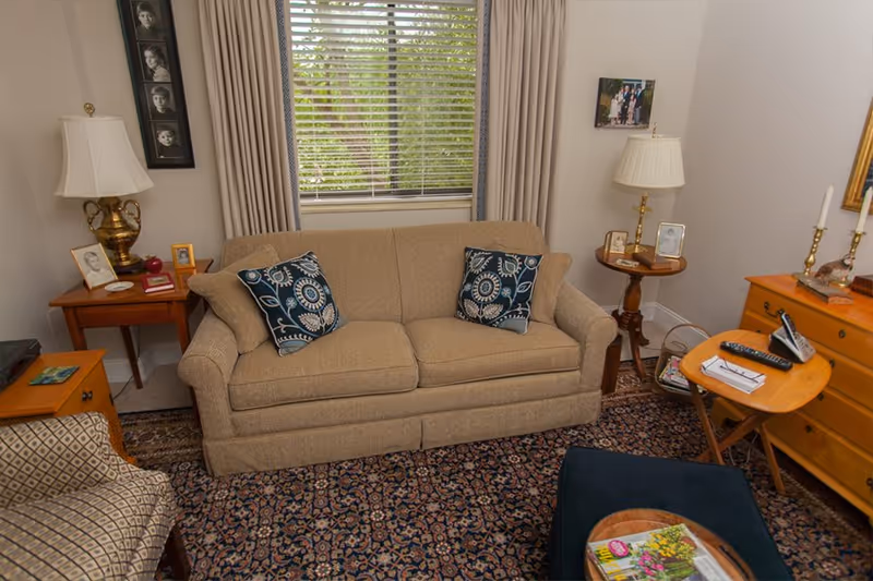 Cozy living room with a beige sofa and patterned pillows between side tables and lamps beneath a window with curtains.