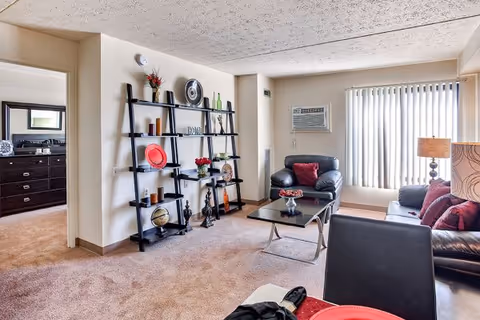 Cozy living area with black leather sofas, a glass coffee table, and a decorative shelf.