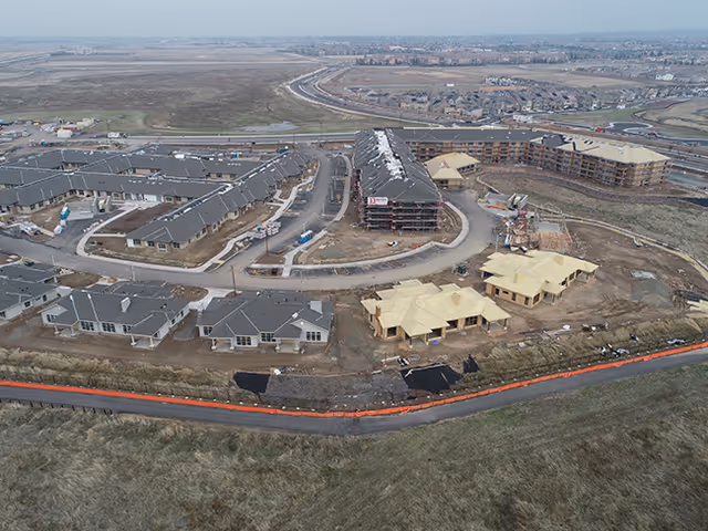 Aerial view of a large assisted living and memory care facility under construction, showing multiple buildings at various stages of completion surrounded by roads and open land.
