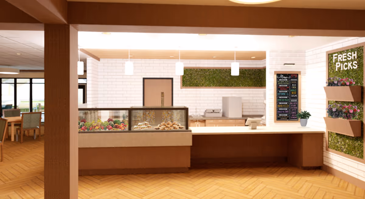 Interior view of a food service counter area in a senior living facility with a display case containing fruits, sandwiches, and cookies. The counter has a cash register, and there is a menu board on the wall. To the right, a vertical garden wall with the words 'Fresh Picks' and flower pots is visible. Dining tables and chairs are seen in the background.