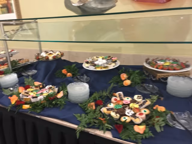 Buffet table displaying plates of decorated cookies and small desserts arranged on a blue cloth under a glass sneeze guard.