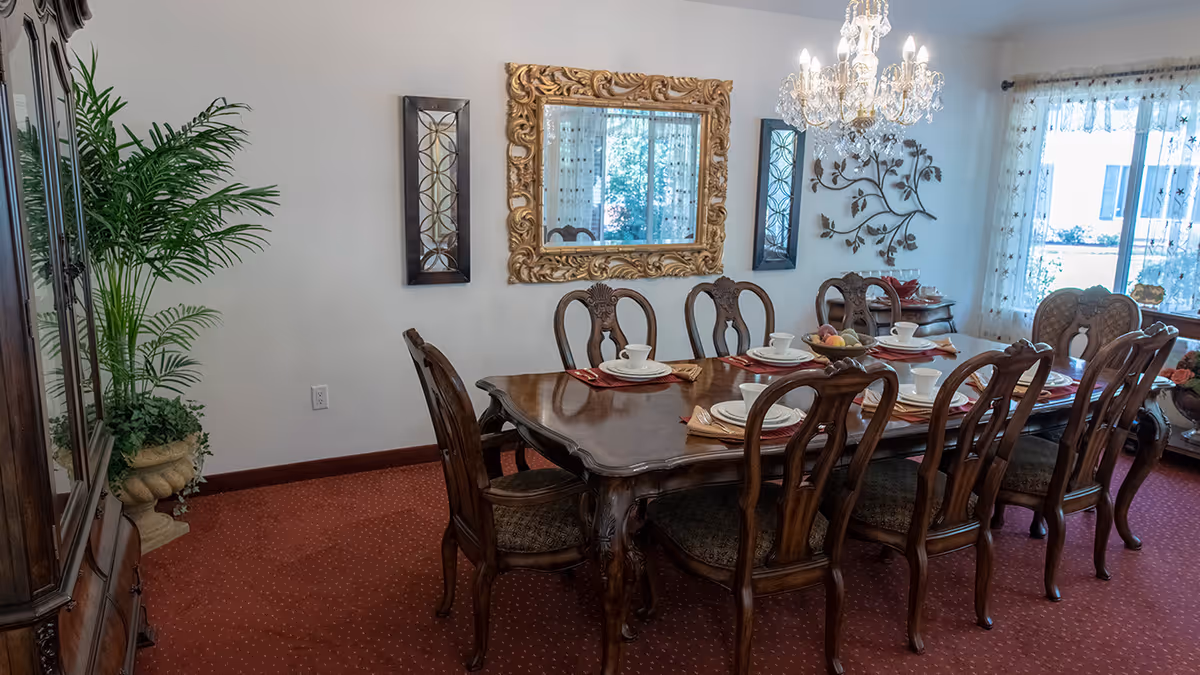 Formal dining room with a long carved wooden table set with dishes, matching chairs, a chandelier, and a large gilded mirror.