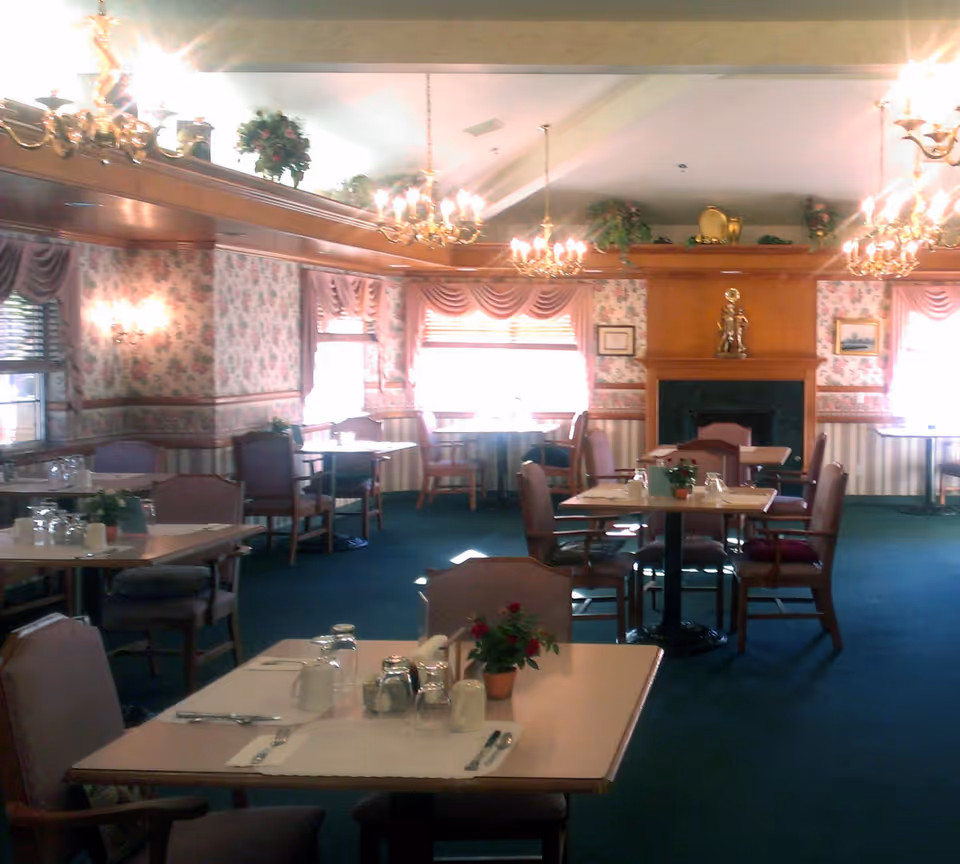 Formal dining room with multiple set tables and chairs, chandeliers, floral wallpaper, and a fireplace at the far wall.
