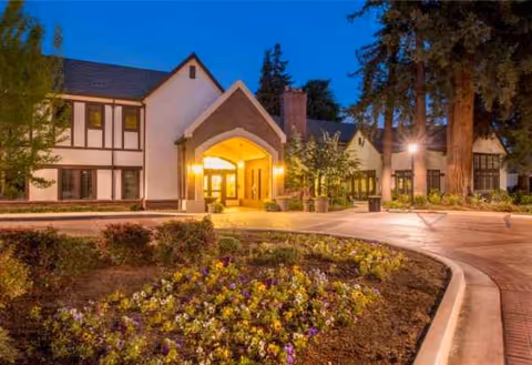 Front exterior of Villa Siena Senior Living Community at dusk with illuminated entrance and gardens.