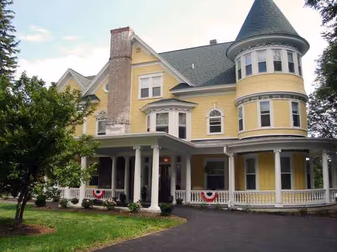 Yellow Victorian-style senior living facility with turret, wraparound porch, and manicured lawn.