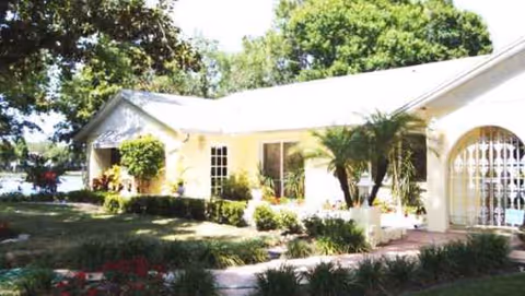 White, single-story building with arches and manicured garden in front.