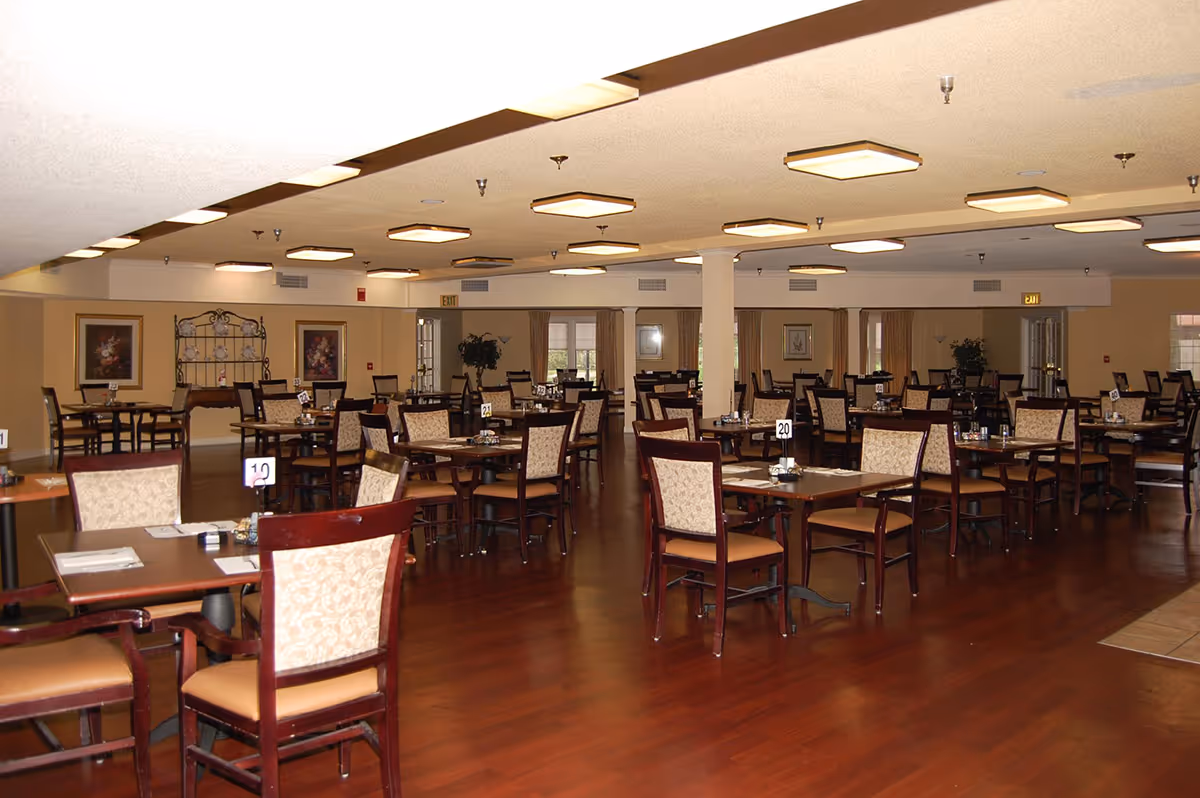 Spacious dining room with multiple tables and upholstered chairs arranged on hardwood floors under ceiling lights.