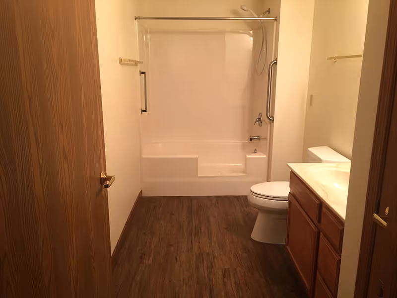 A clean bathroom with a bathtub/shower combo, toilet, sink vanity, and wood-look flooring.