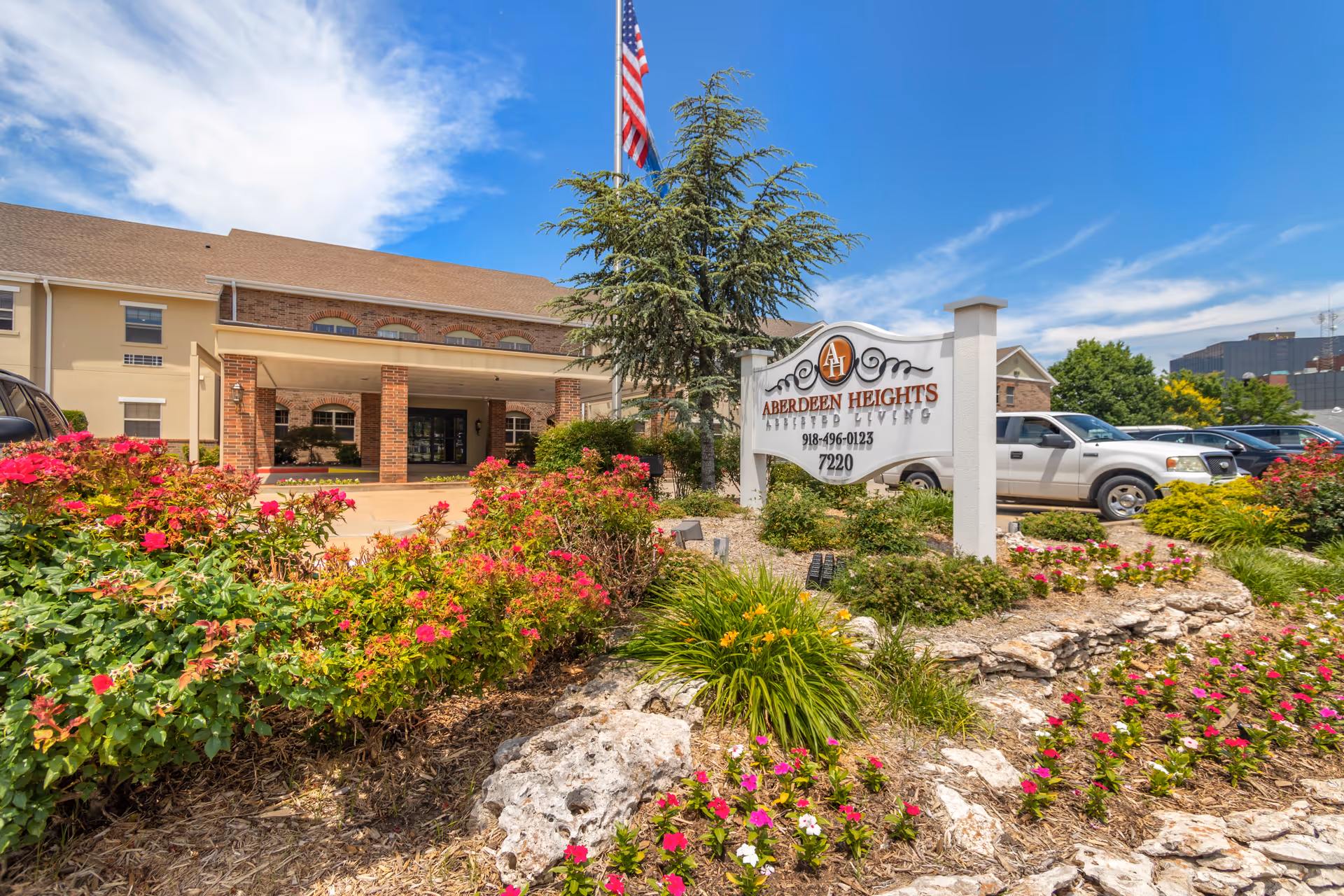 Front entrance of Aberdeen Heights Assisted Living with a sign and landscaped flowerbeds under a blue sky.