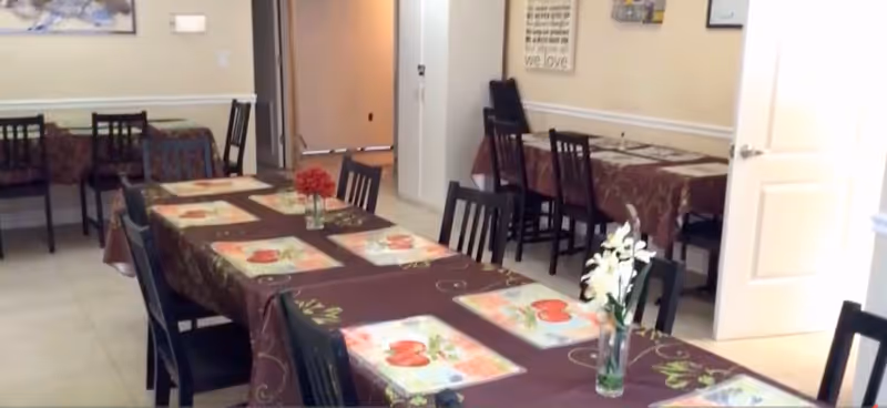 Communal dining room with several tables and chairs set with placemats and small floral centerpieces.