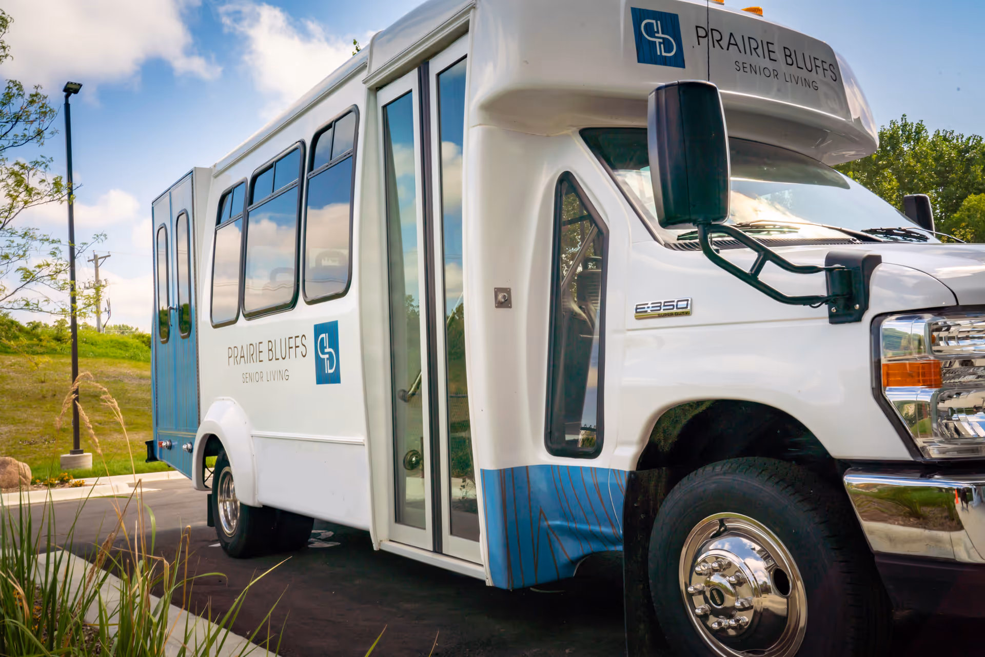 White Prairie Bluffs Senior Living shuttle bus parked outdoors near landscaping.