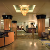 Elegant senior living lobby with large round columns, a tiered chandelier, reception desks, seating areas, and marble floors.