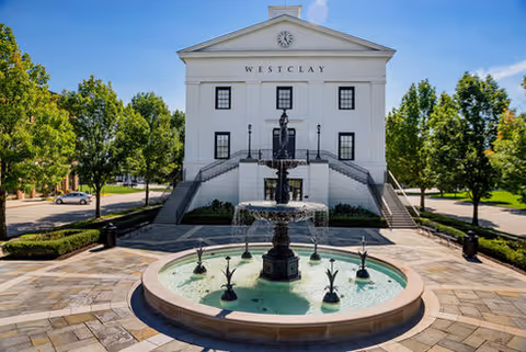 Front view of the white Westclay building with a tiered fountain and stone plaza framed by trees.