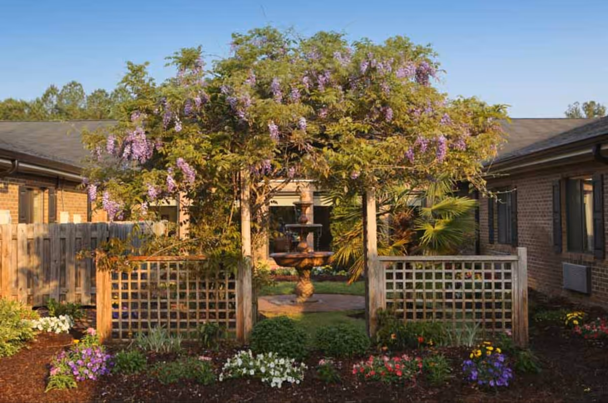 Outdoor garden courtyard at a senior facility with a central fountain and flowering plants.