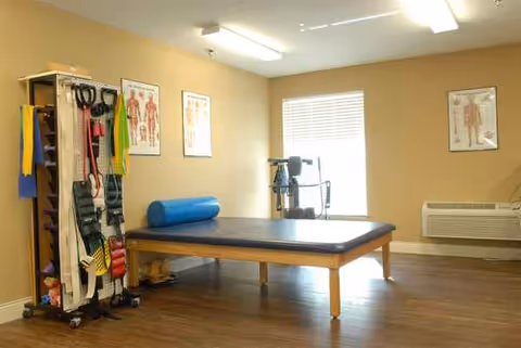 A therapy room with a wooden treatment table, exercise bands, and wall charts.