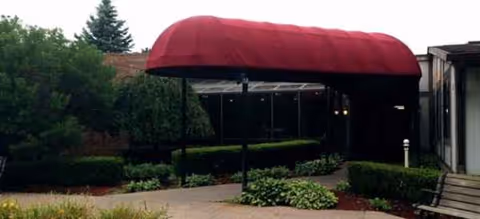 Exterior view of a building entrance with a red arched canopy and landscaping.