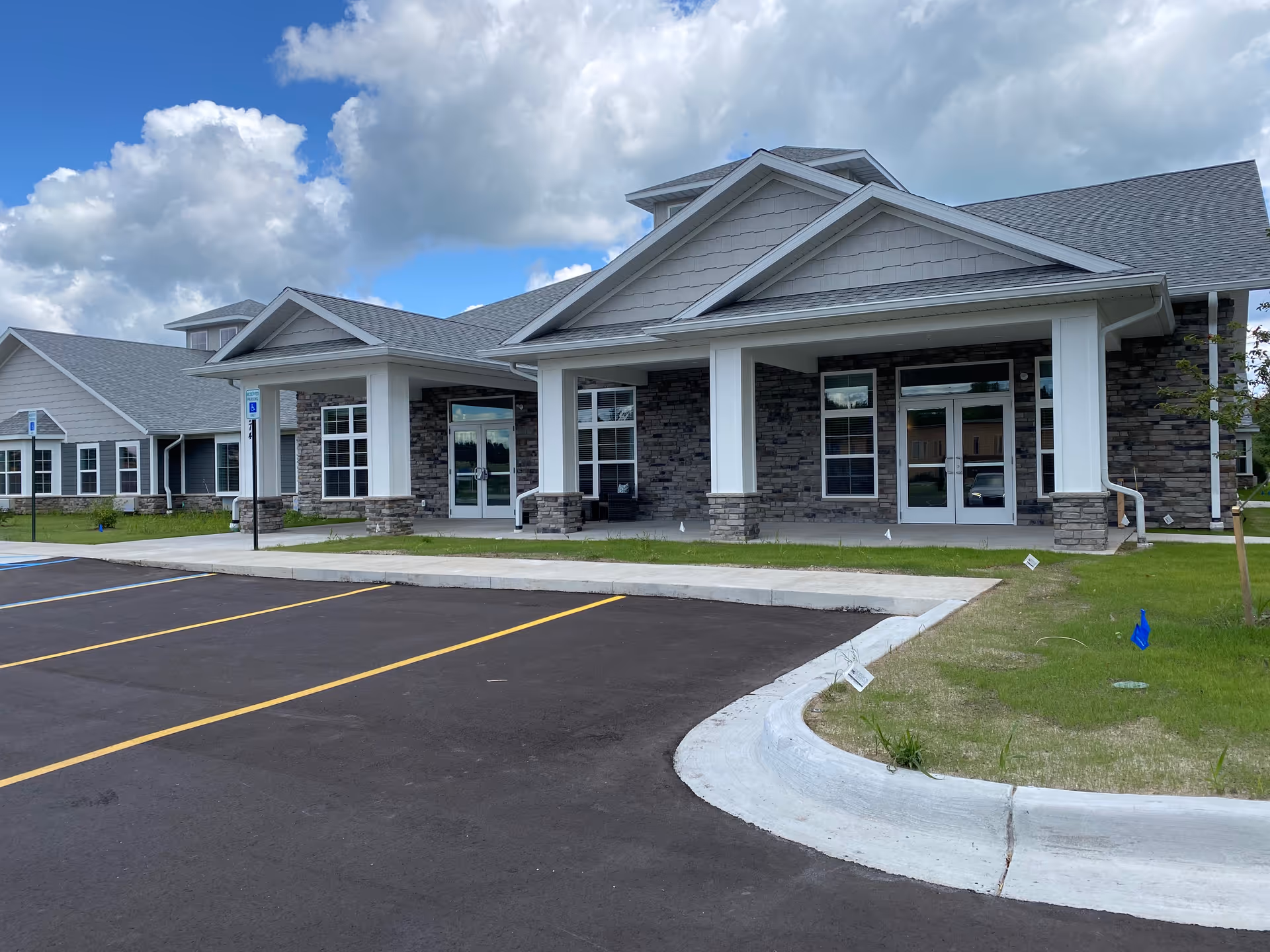 Exterior view of Beacon Pointe Assisted Living facility in Richland showing a modern building with stone and siding facade, large windows, covered entrance, and an empty parking lot under a partly cloudy sky.