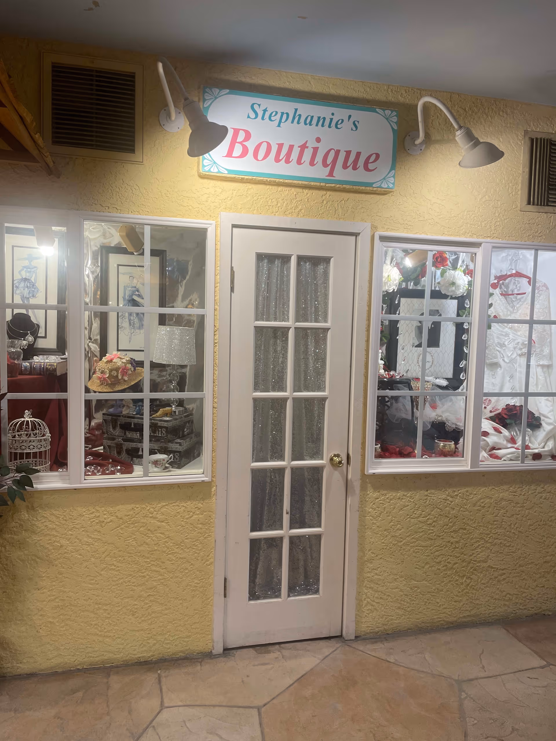 Interior storefront sign reading 'Stephanie's Boutique' above a white multi-pane door flanked by display windows showing hats and decorative items.