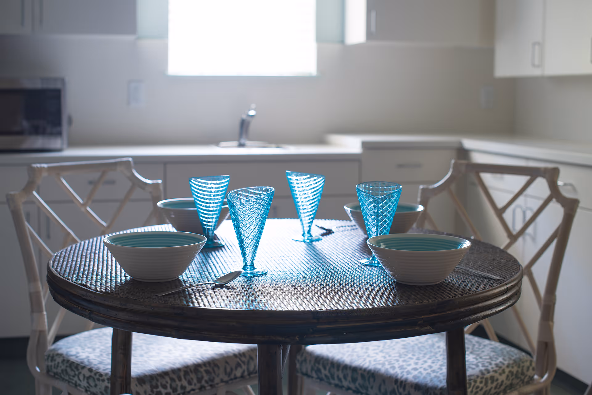 Round dining table set with turquoise glass goblets and bowls in a bright kitchen nook.