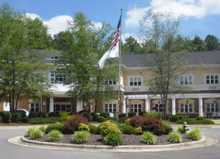 Front entrance of a senior living building with a circular driveway, landscaped island and an American flag flying in front.