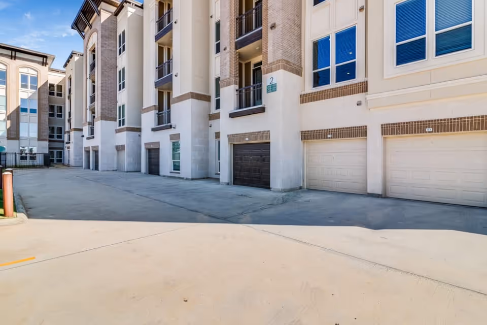 Exterior view of a multi-story residential building with several garage doors at ground level and balconies on the upper floors under a clear blue sky.