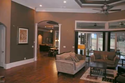 Spacious senior living lounge with sofas, coffee table, ceiling fan, and large windows.