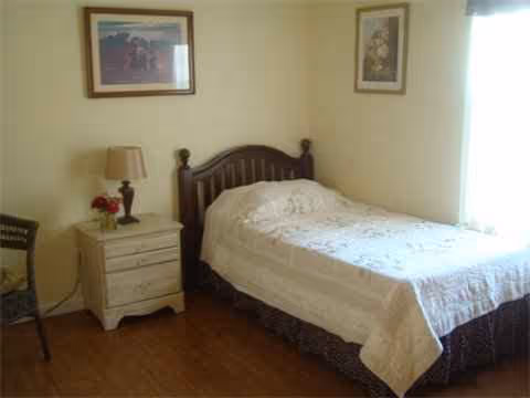 A small bedroom featuring a wooden bed, nightstand, lamp, and framed wall art.