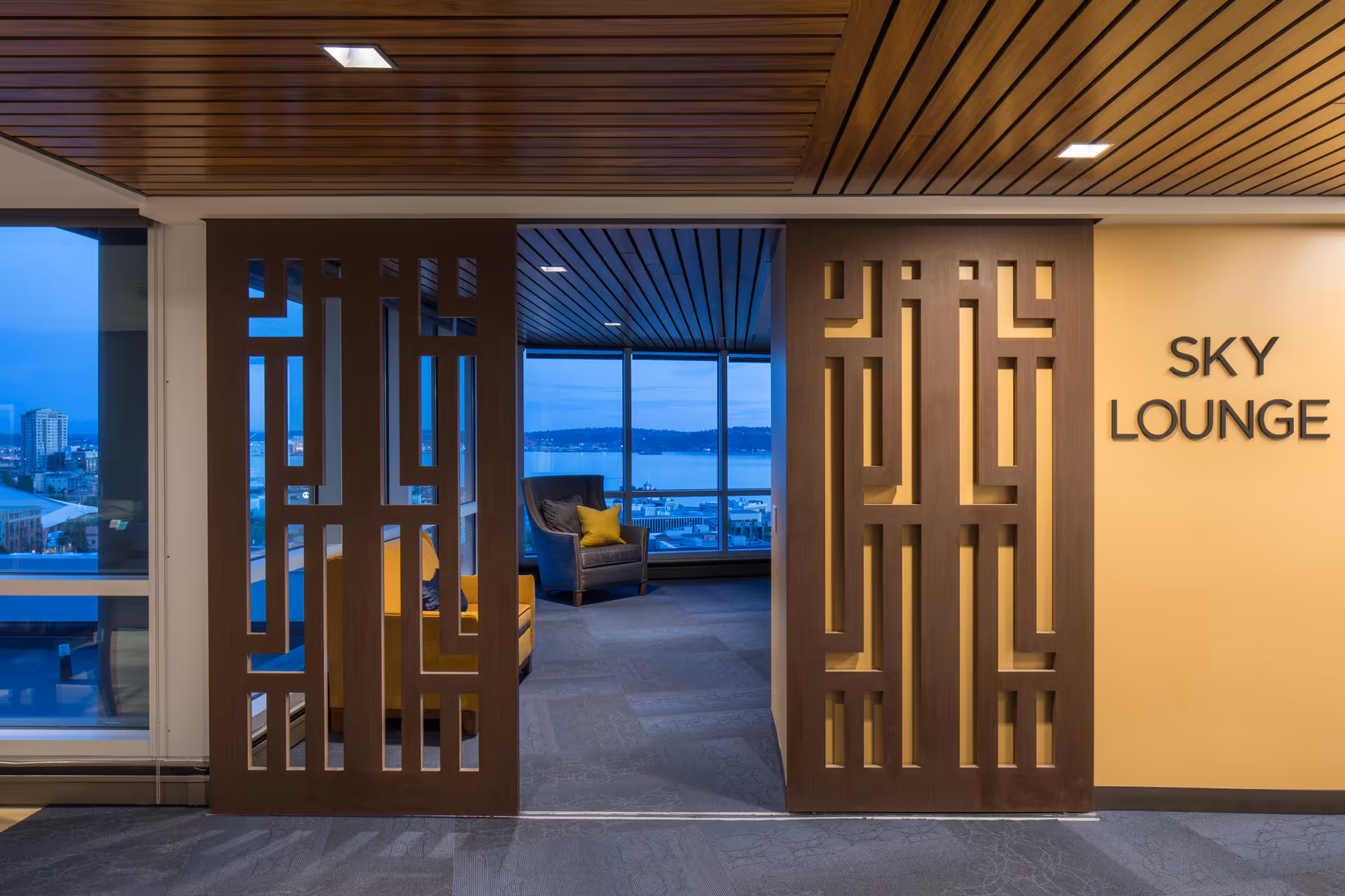 Entrance to a sky lounge with decorative wooden partitions, upholstered seating and large windows overlooking a waterfront view.