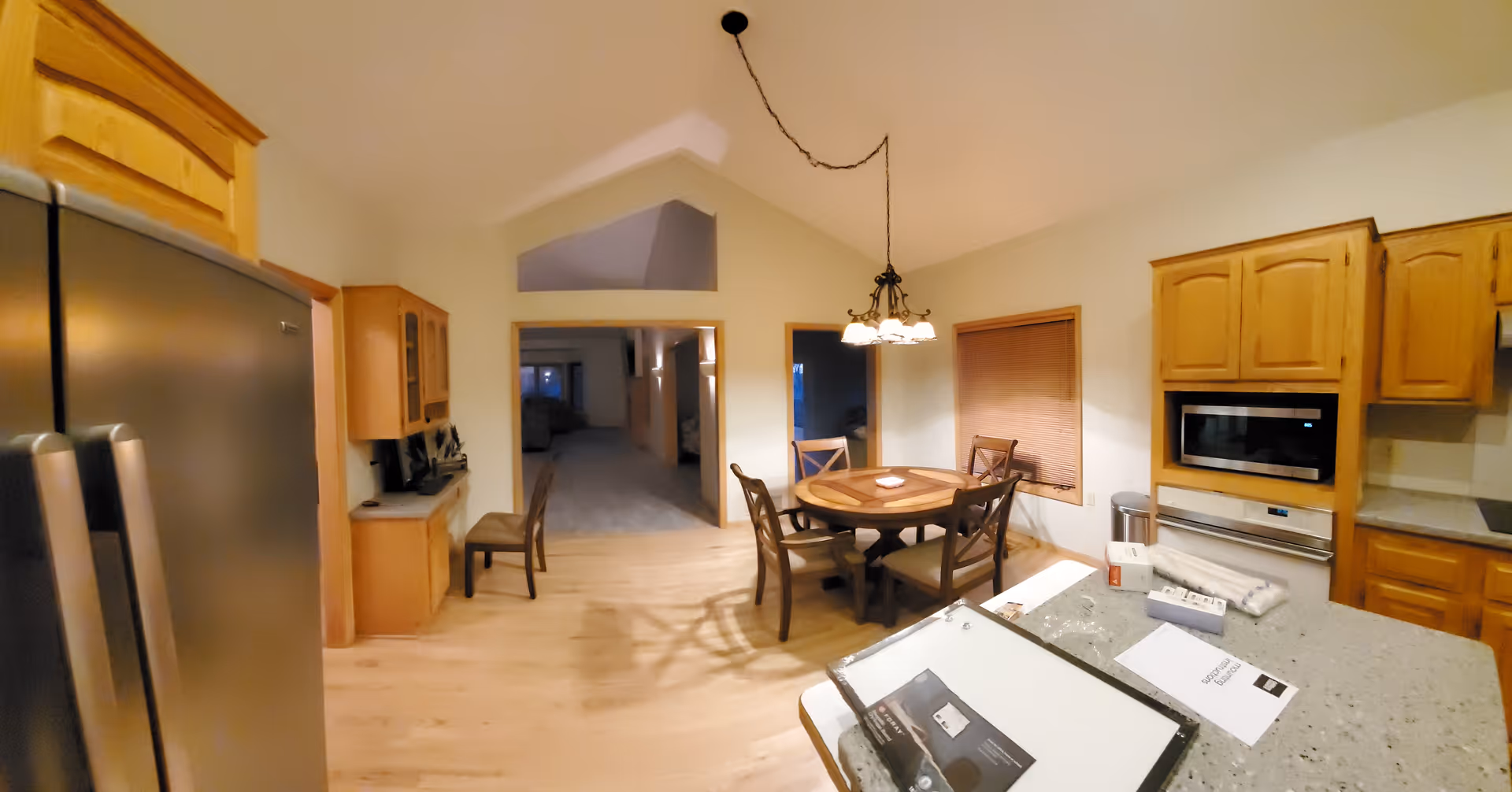 Open kitchen and dining area with wooden cabinets, a round dining table, and a countertop island with papers.
