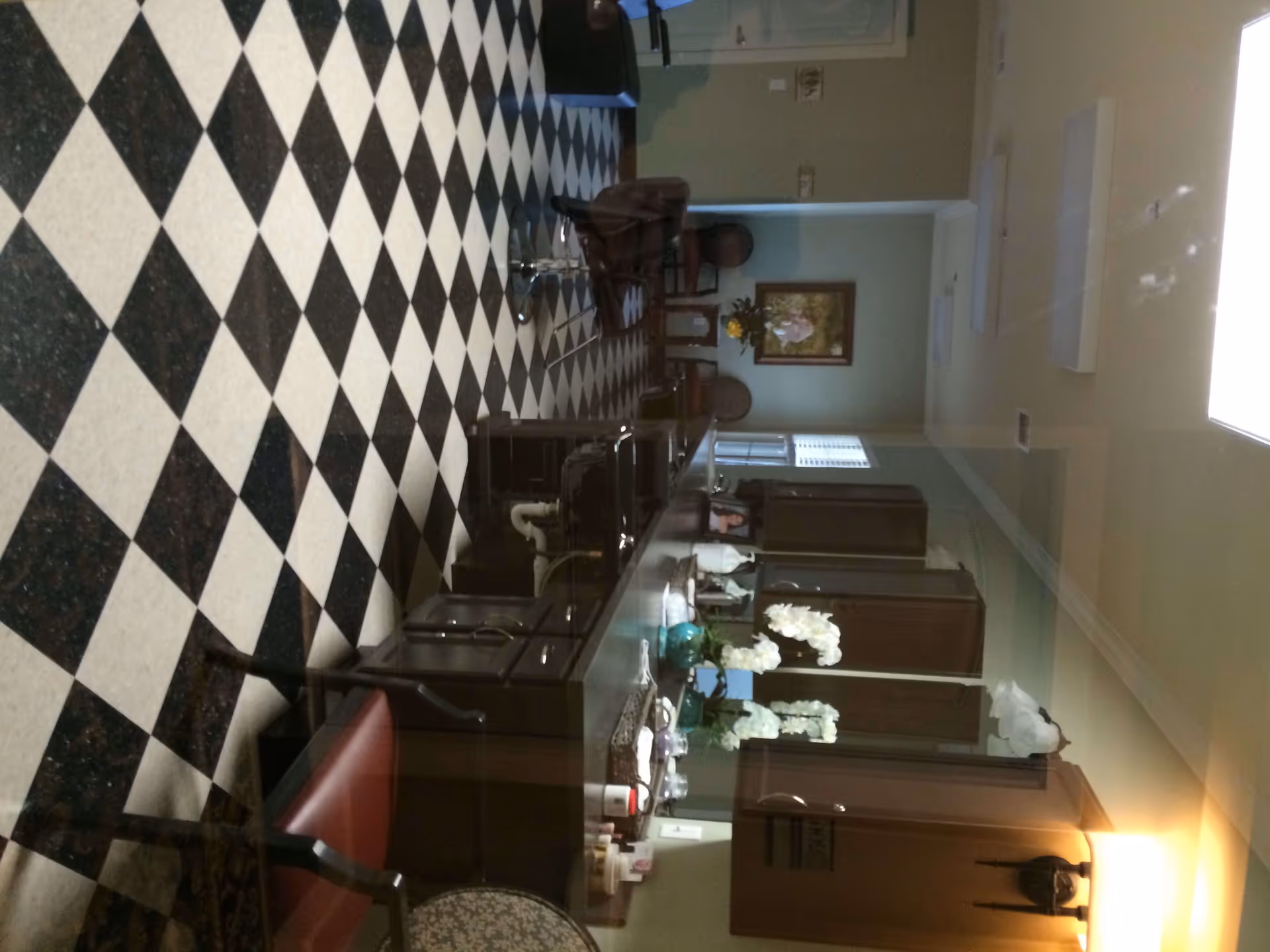 Interior room with a black-and-white checkered floor, a long counter and cabinets, salon chairs and floral arrangements.