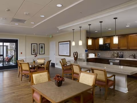 Open dining area with multiple tables and chairs and a breakfast bar with pendant lights and a kitchen in the background.