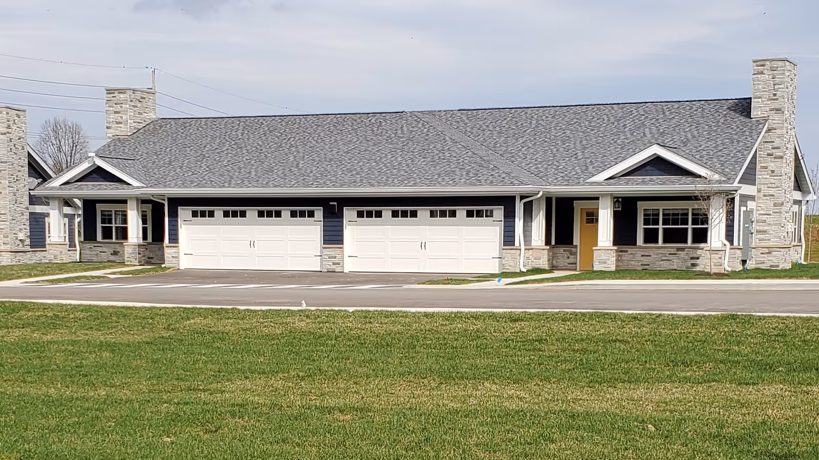 Single-story senior living facility with stone detail and three-car garage, grassy foreground.
