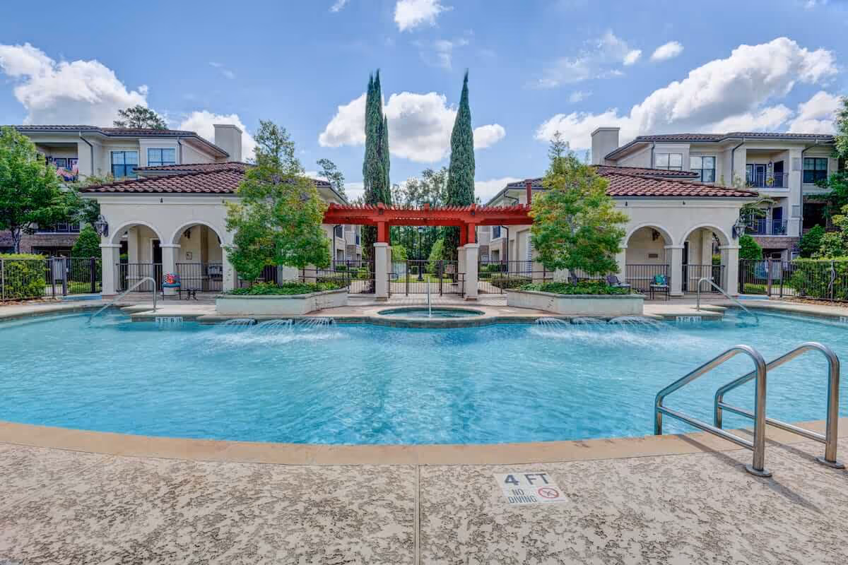 Outdoor swimming pool and courtyard with a red pergola and surrounding apartment-style buildings.