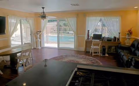 Bright yellow living area with sheer white curtains, pool view, and desk workspace.